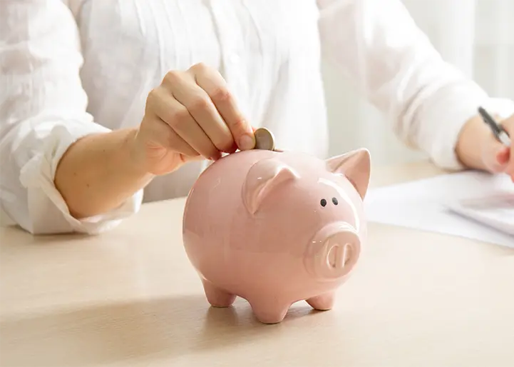 A person putting a coin on a piggy bank.